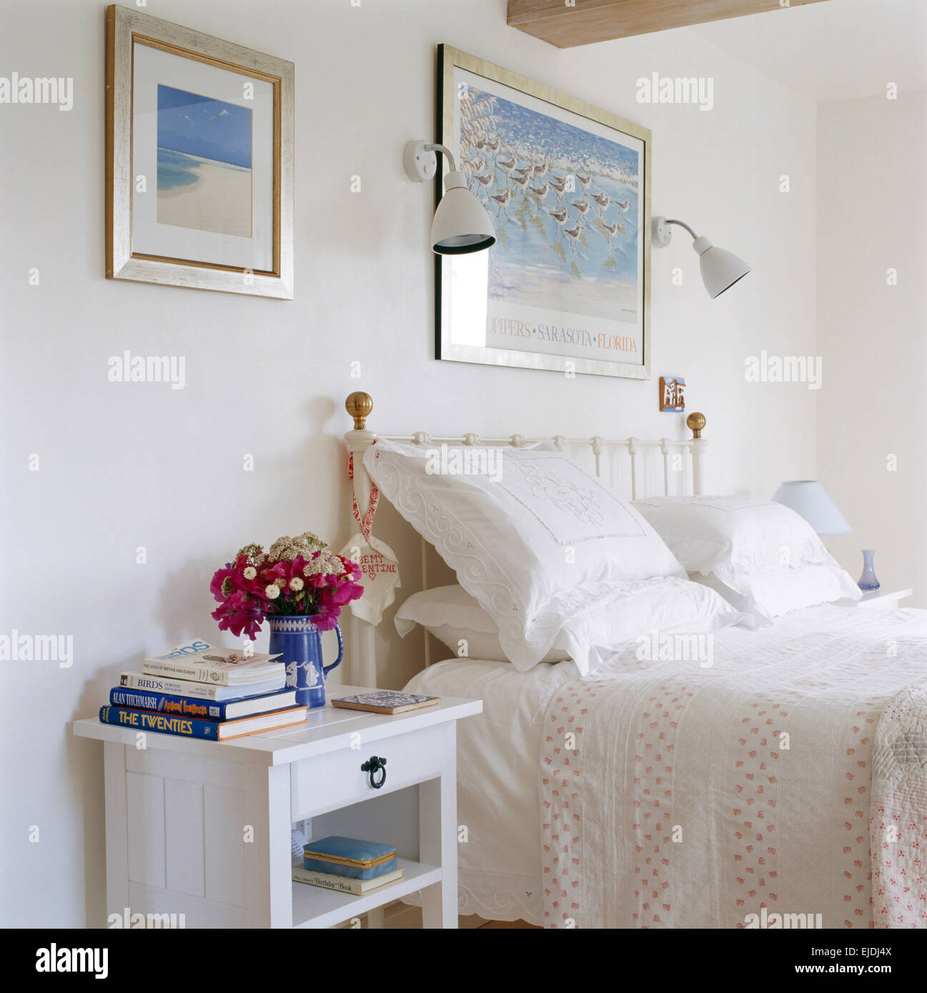 Vaso di fiori d'estate sulla tavola dipinta accanto al letto di ottone con biancheria bianca e cuscini letto macchiato il coperchio Foto Stock
