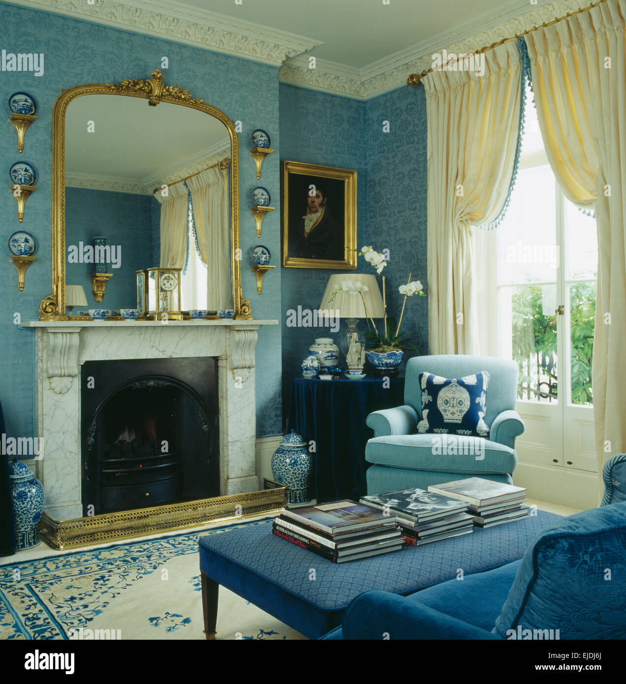 Grande specchio dorato sopra caminetto in marmo in blu la stanza di seduta con crema di tende sulla finestra Foto Stock