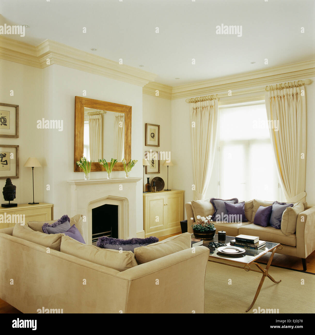 Malva di cuscini di seta su divani color crema in elegante residenza di città la stanza di seduta con specchio sopra il camino Foto Stock