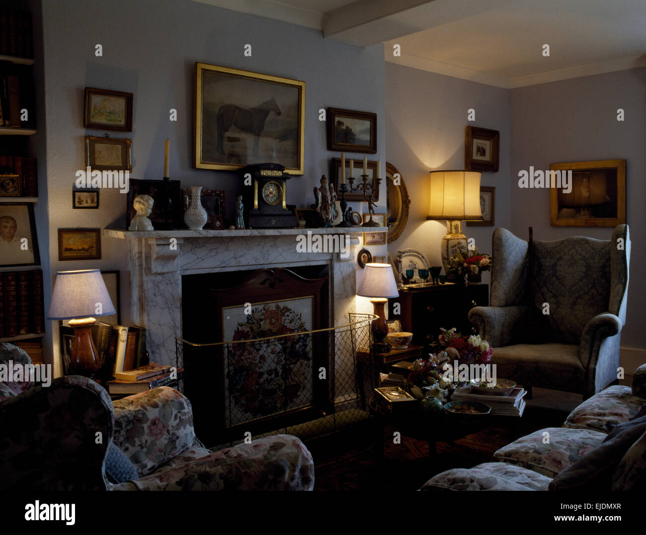 Lampade illuminate e camino in marmo con metallo fireguard nel confortevole salotto Foto Stock