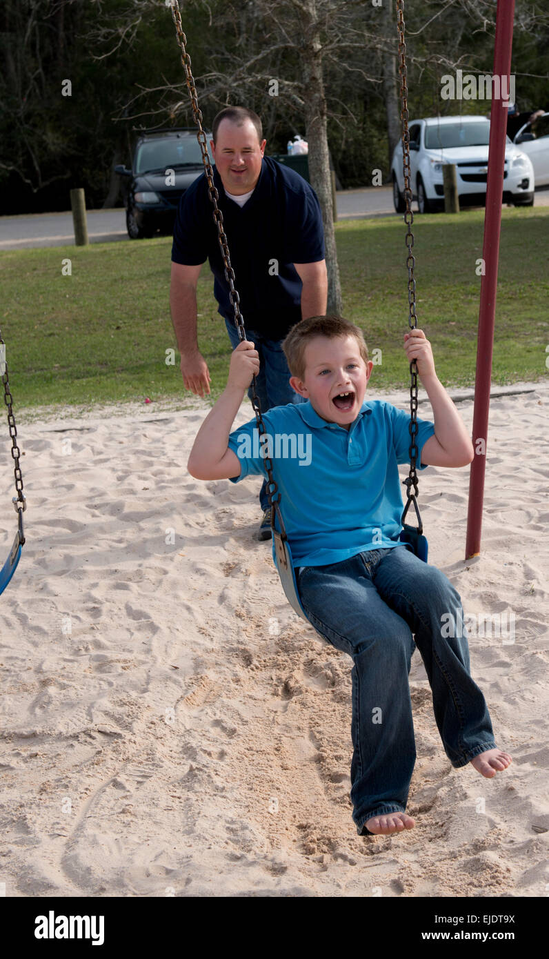 Papà spinge il bambino di otto anni su swing sul parco giochi per bambini Foto Stock