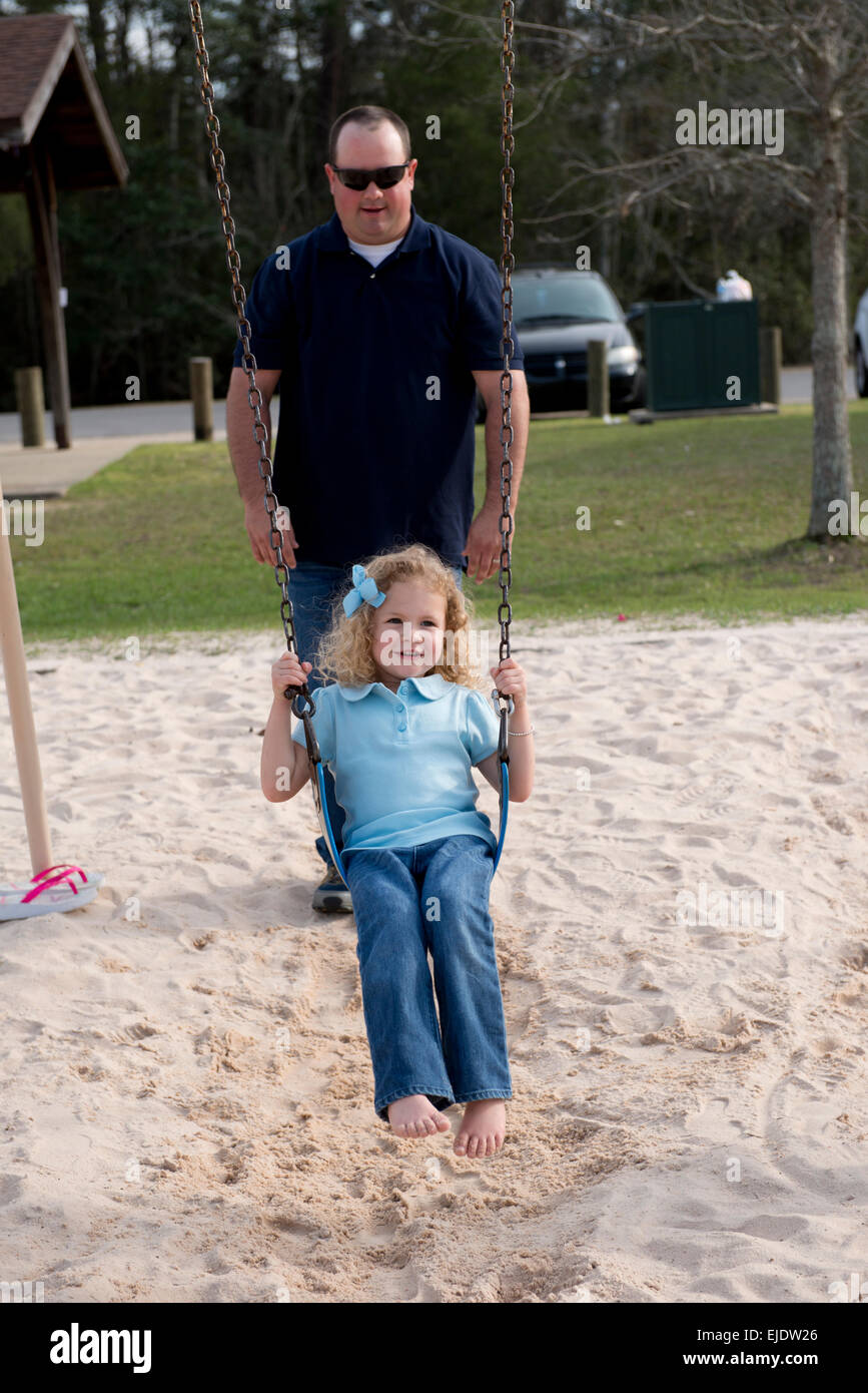 Papà oscillando la sua quattro anni alla figlia di un parco giochi per bambini Foto Stock