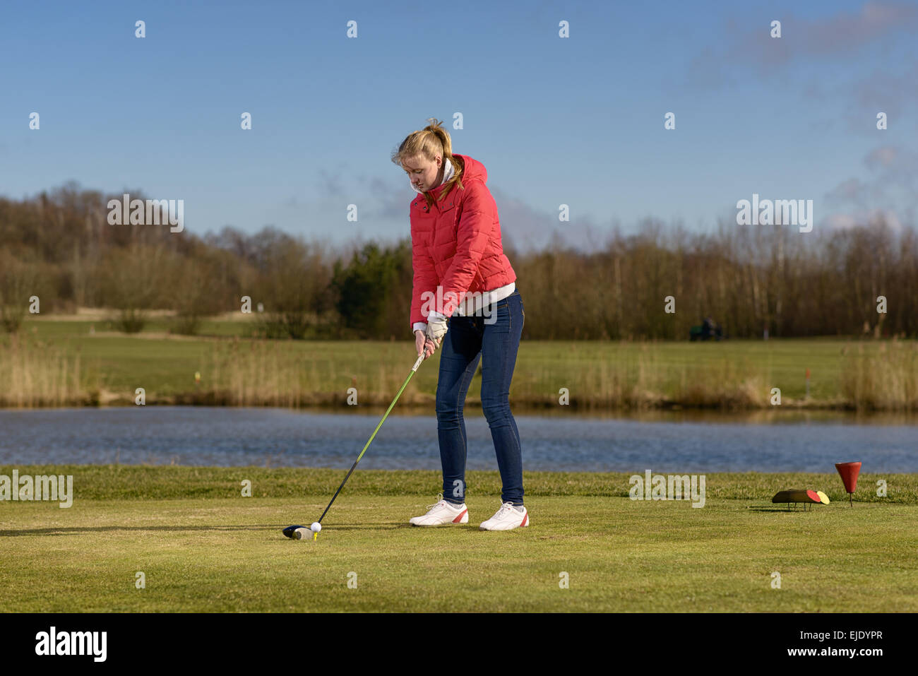 Donna di rinvio su un campo da golf in piedi nella scatola a t di fronte a un pericolo in acqua con un autista nelle sue mani Foto Stock