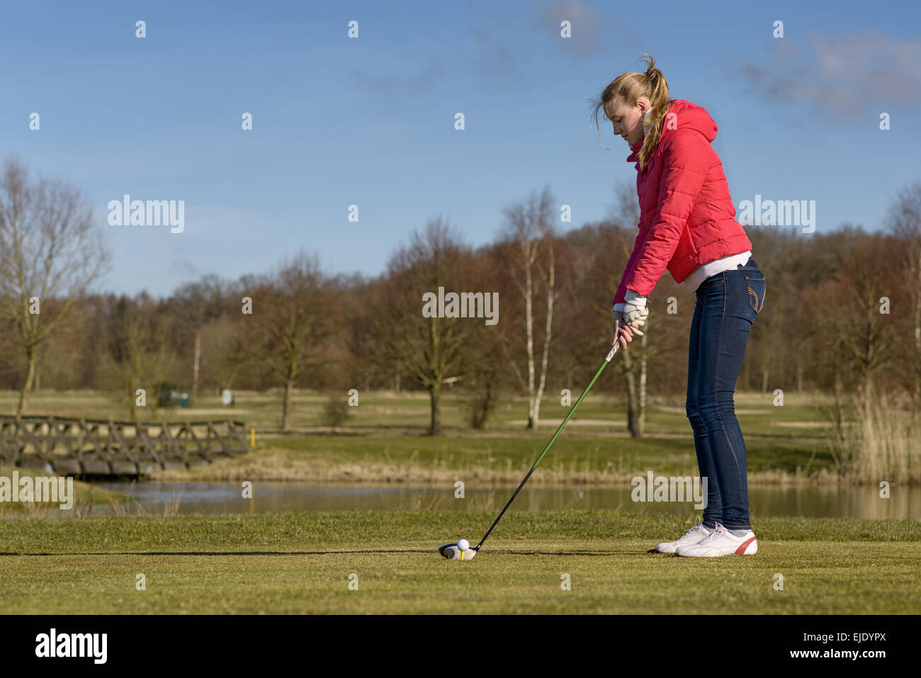 Donna di rinvio su un campo da golf in piedi nella scatola a t di fronte a un pericolo in acqua con un autista nelle sue mani Foto Stock