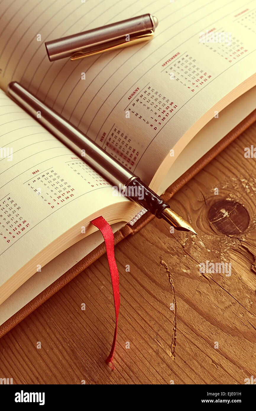 Aprire il diario con una penna stilografica in esso, posto su una tavola di legno. Elaborazione vintage. Foto Stock
