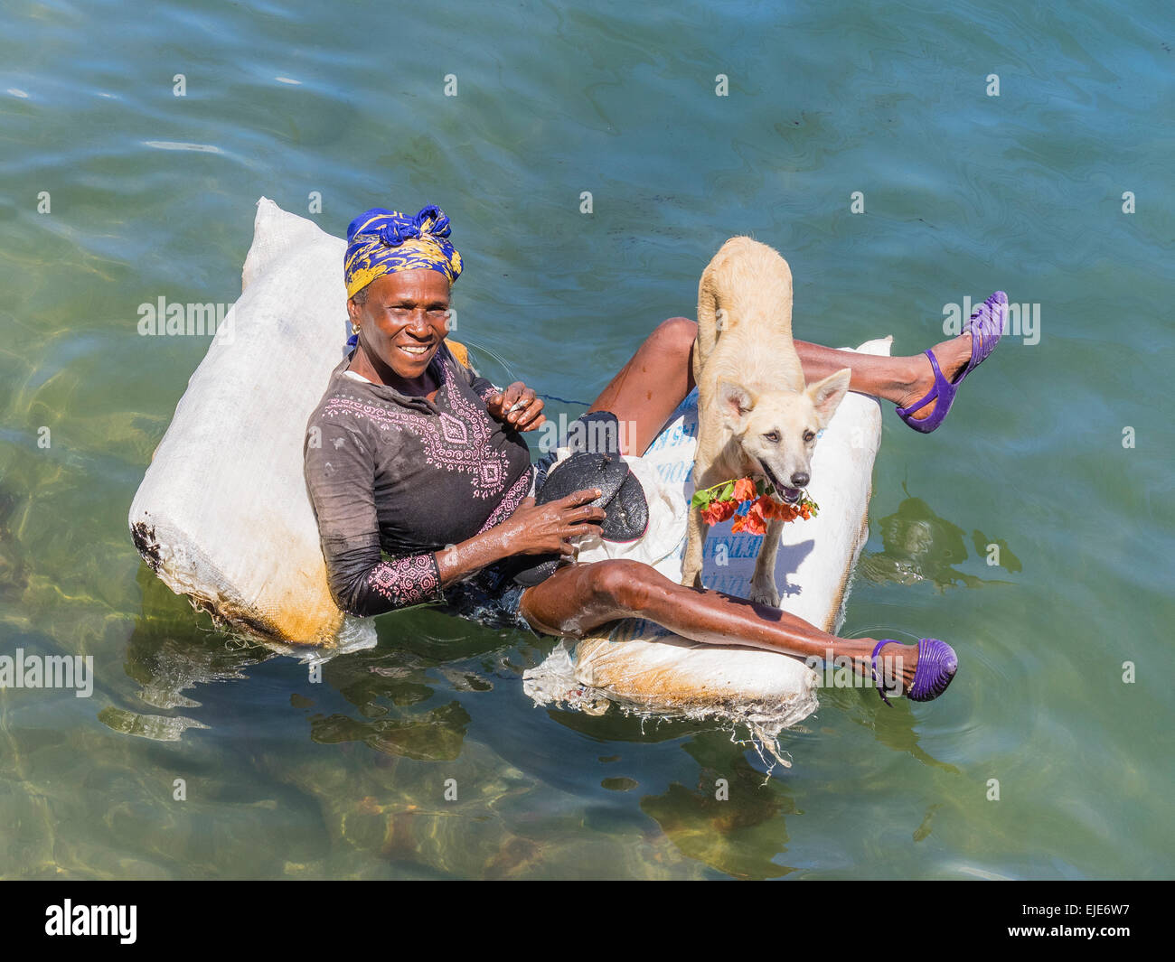 Una femmina di afro-cubane mendicante sdraiato su una zattera nell'oceano di Cayo Granma. Ella è accompagnato dal suo cane bianco. Foto Stock