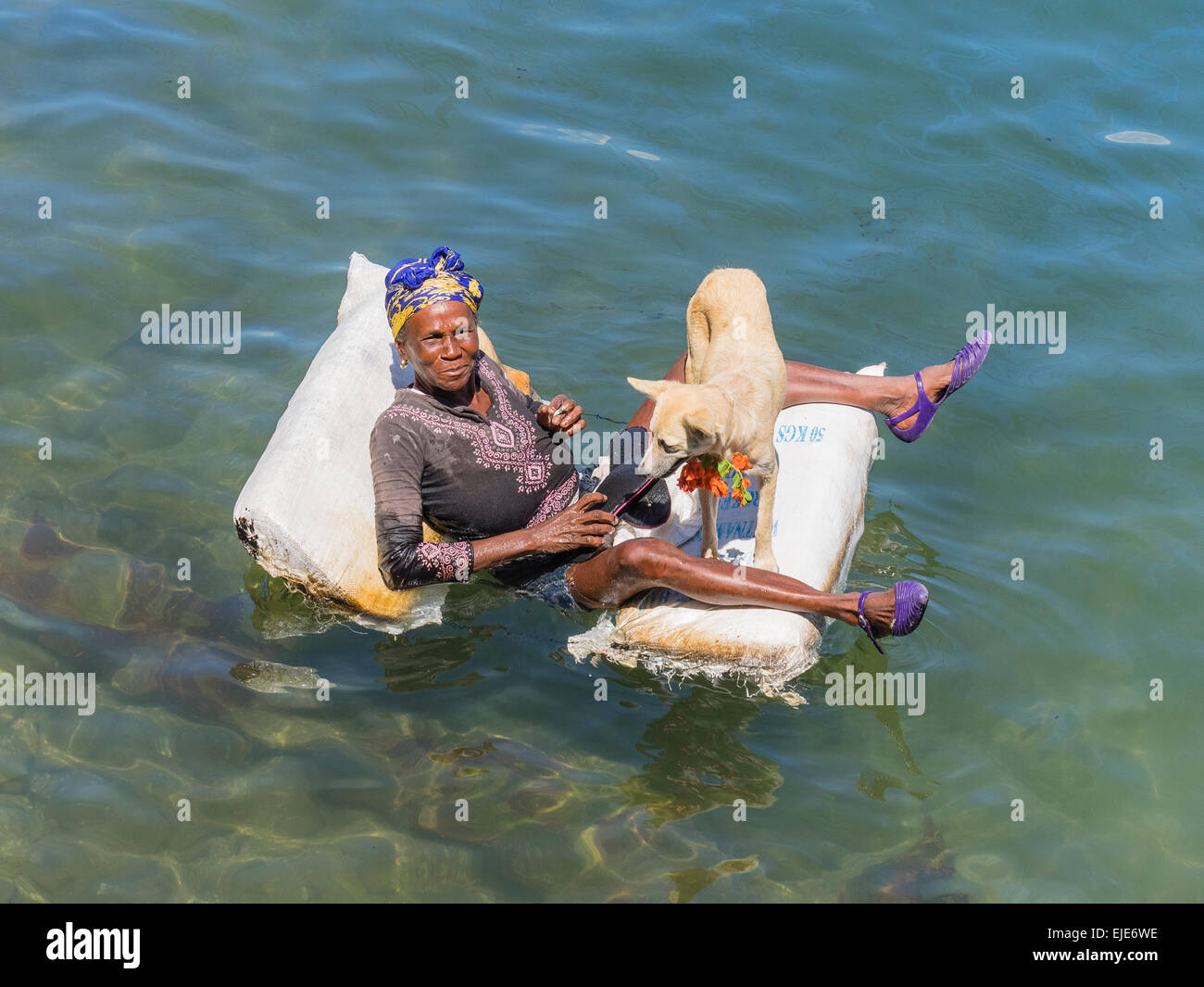 Una femmina di afro-cubane mendicante sdraiato su una zattera nell'oceano di Cayo Granma. Ella è accompagnato dal suo cane bianco. Foto Stock