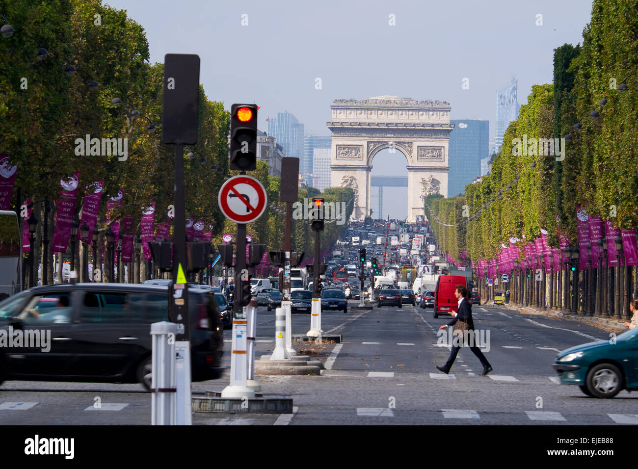 Un uomo cammina alacremente attraverso gli Champs Elysees di Parigi in Francia con la mitica Arc Du Triomphe in distanza. Foto Stock