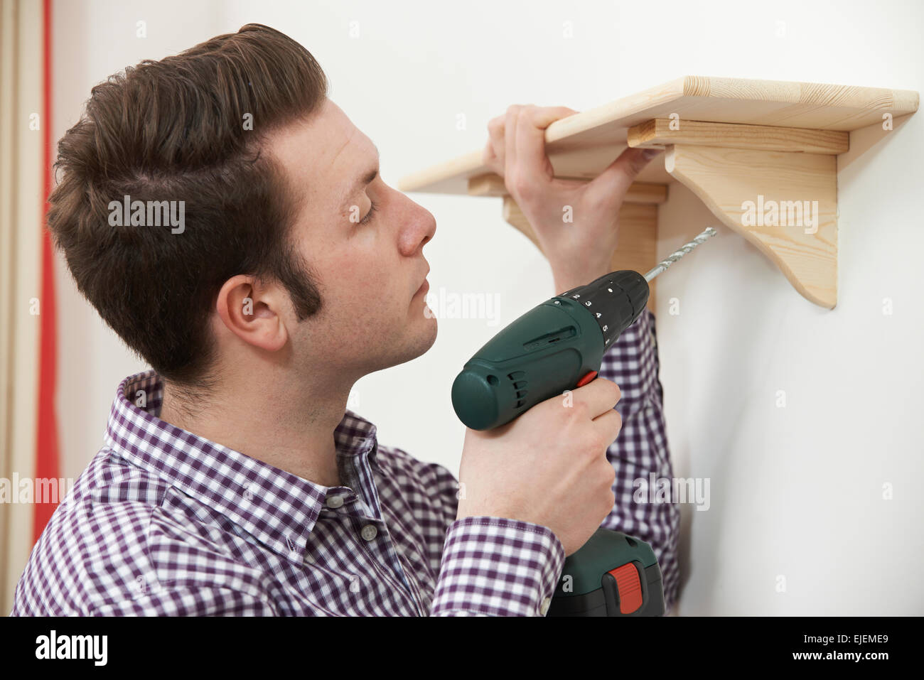 L'uomo la messa a scaffale di legno di casa utilizzando elettrico trapano cordless Foto Stock