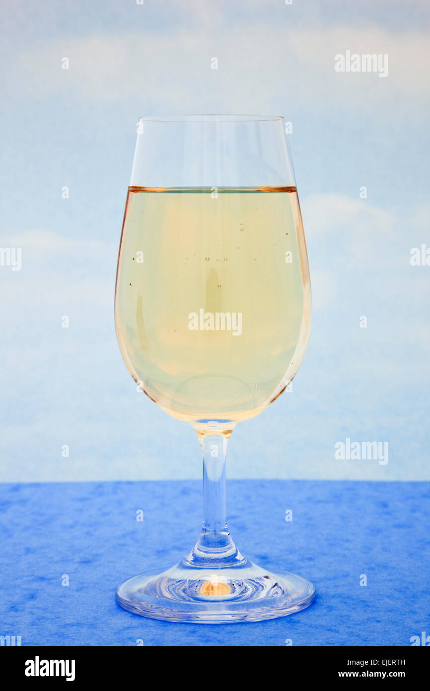 Bicchiere di vino bianco su un tavolo blu con un cielo blu sullo sfondo Foto Stock