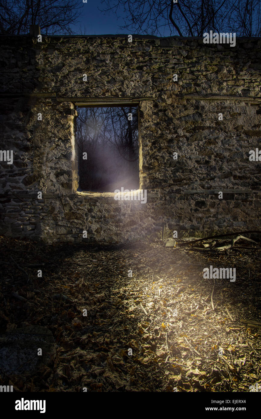 Luce che risplende attraverso la finestra nel vecchio muro di pietra di notte Foto Stock