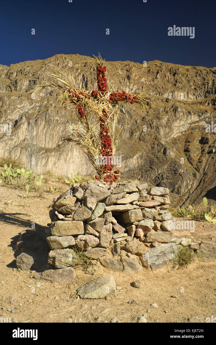 Una croce cristiana avvolto intorno con fiori sul peruviano arido paesaggio nei pressi di Canon del Colca Foto Stock