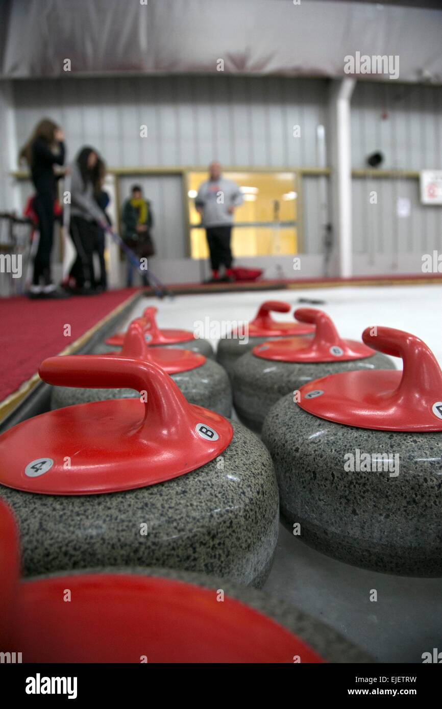 Gruppo di granito pietre di curling sul bordo del Curling su ghiaccio foglio con cureler e spazzatrici in attesa in background. Foto Stock