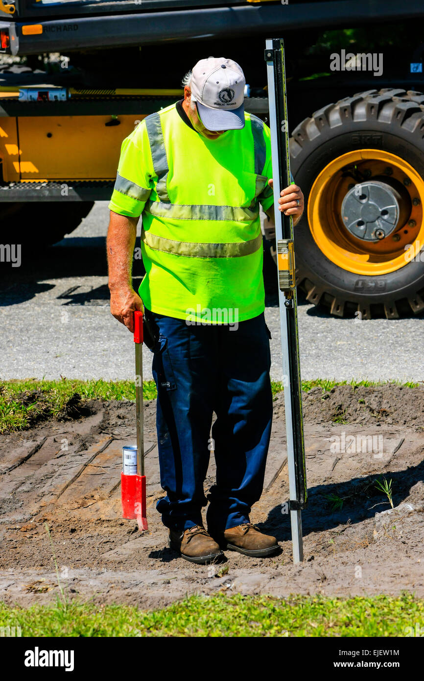 Autostrada lavoratore di manutenzione utilizzando una profondità digitale guage come il retroescavatore rimuove il terreno come parte dell'acqua piovana soak-lontano il drenaggio Foto Stock