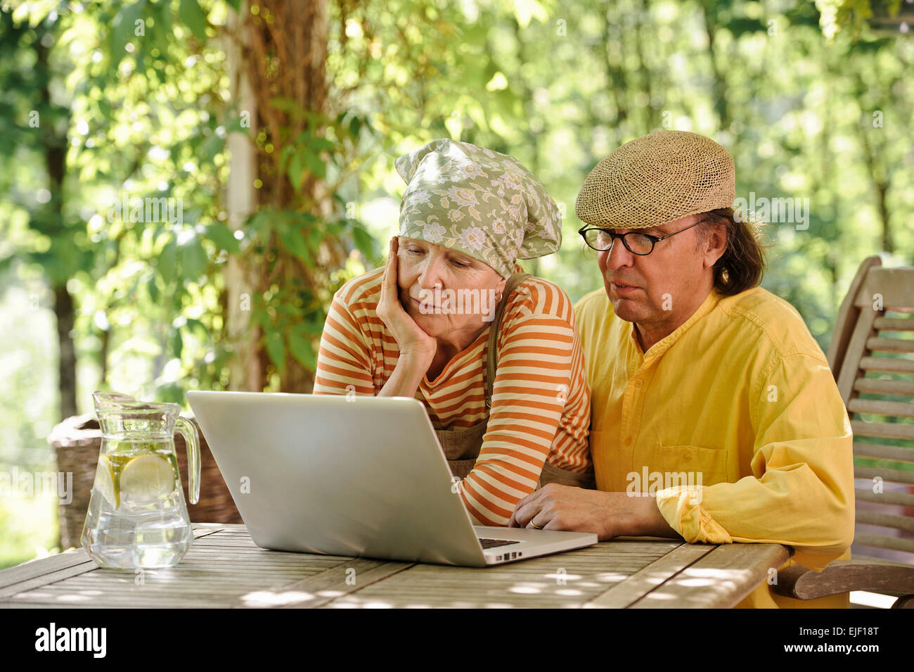 Coppia senior all aperto con un laptop, stanno guardando il computer. C'è una soleggiata sfondo di alberi e cespugli Foto Stock