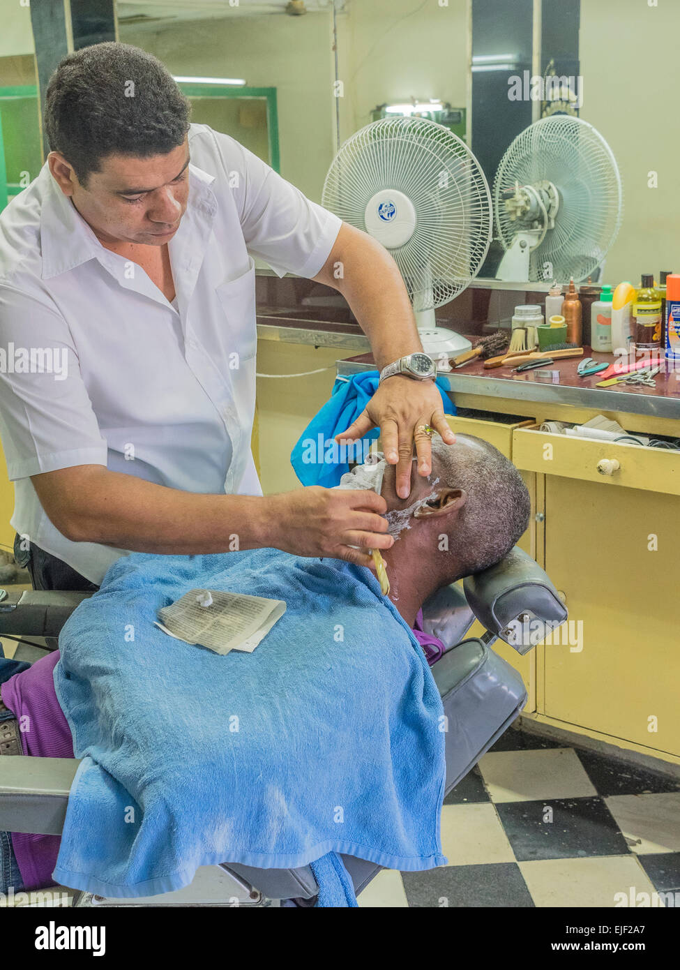 Uomo cubano si stende nel barbiere di sedia e ottiene la rasatura in un barbiere dal barbiere in Santiago de Cuba. Foto Stock