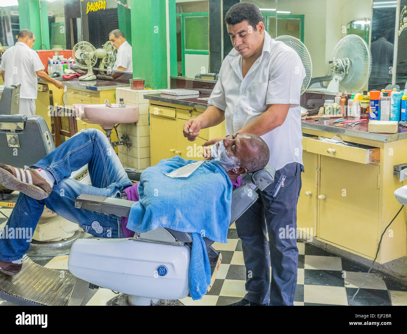 Uomo cubano si stende nel barbiere di sedia e ottiene la rasatura in un barbiere dal barbiere in Santiago de Cuba. Foto Stock