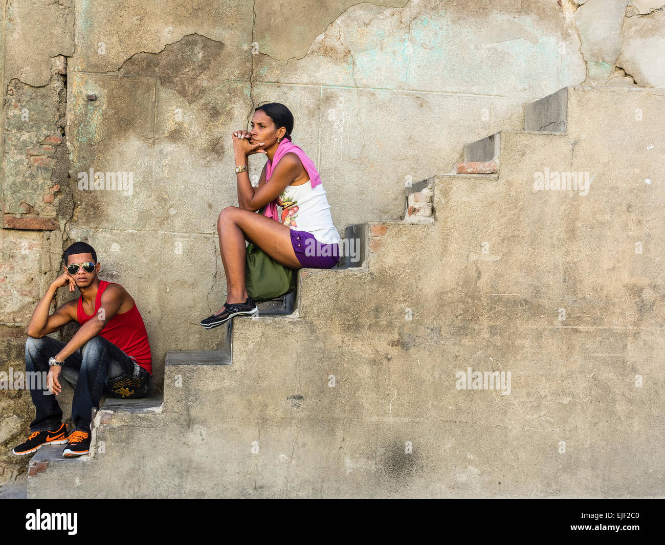 Due persone afro-cubane, uno maschio e uno femmina, sia nel loro 20s, sedersi fuori su una scala di cemento a lato di una casa. Foto Stock