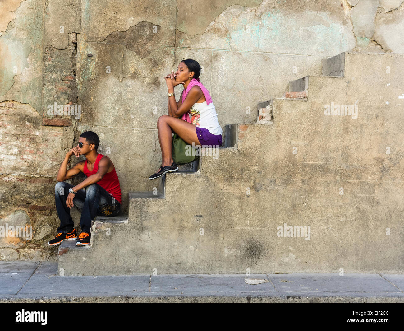 Due persone afro-cubane, uno maschio e uno femmina, sia nel loro 20s, sedersi fuori su una scala di cemento a lato di una casa. Foto Stock
