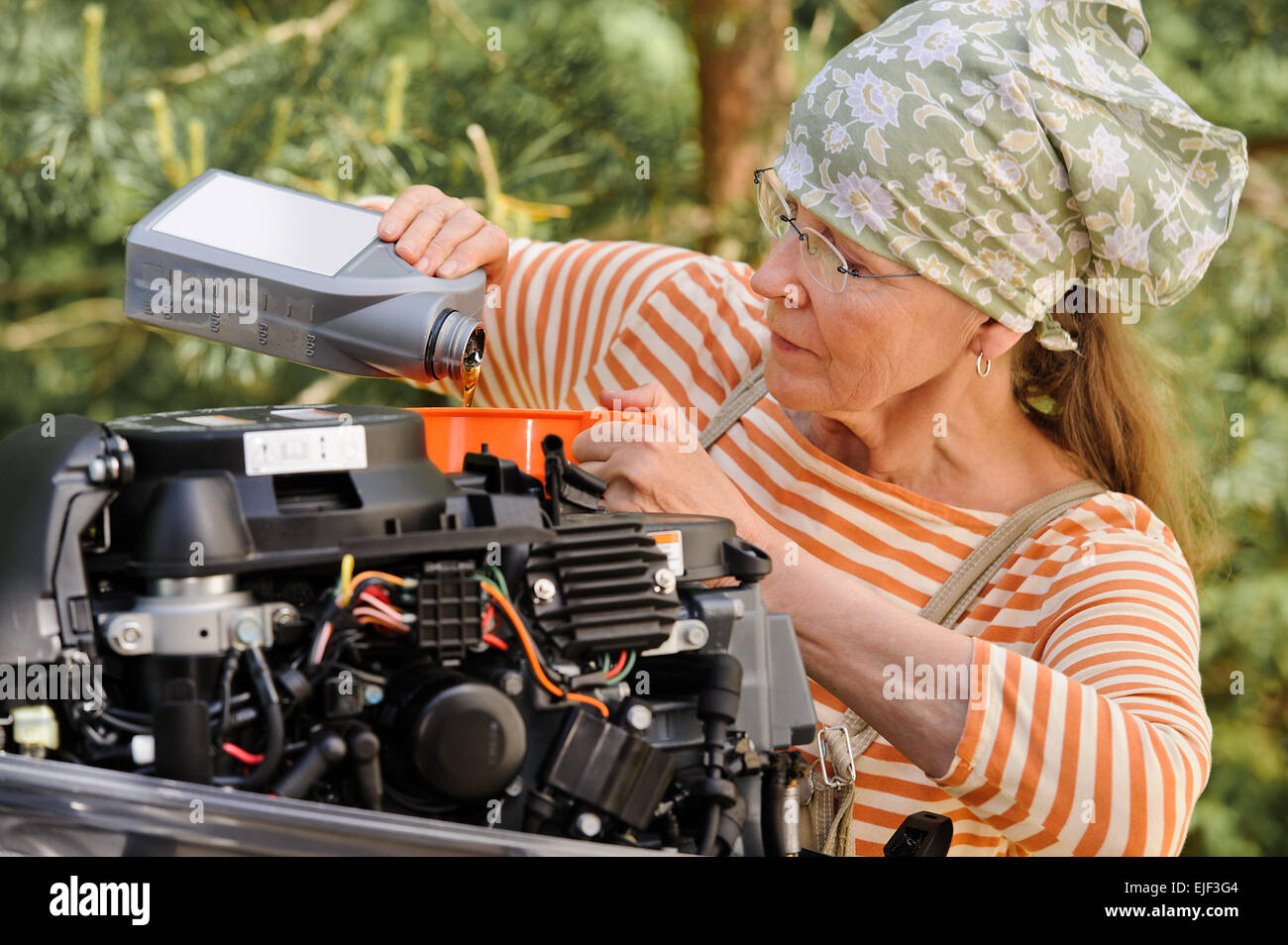 Senior donna versa olio in un motore fuoribordo attraverso un imbuto. Abbattere gli stereotipi della donna - sesso ed età Foto Stock