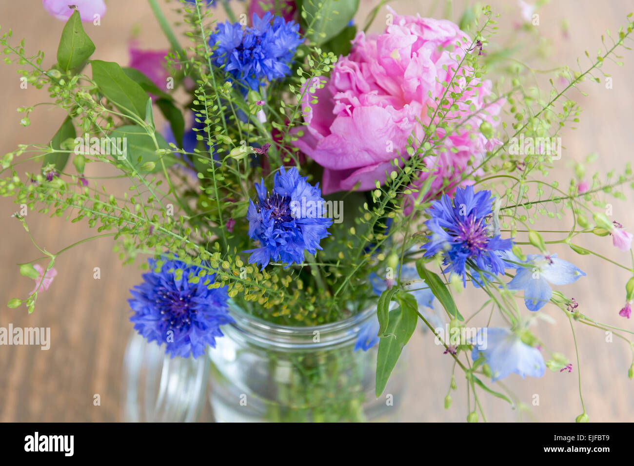 Posy mazzetto di piuttosto attraente colore rosa pastello e molla blu e fiori estivi, un rustico bouquet floreale disposizione in vetro vas Foto Stock