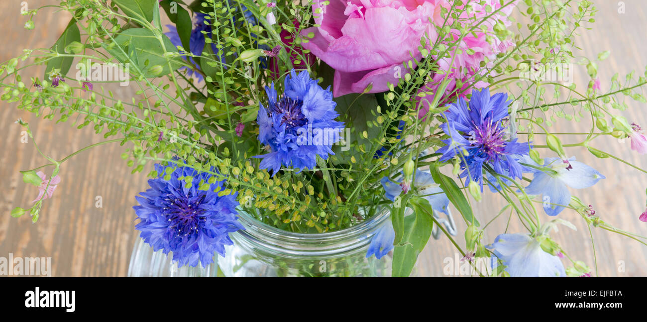 Posy mazzetto di piuttosto attraente colore rosa pastello e molla blu e fiori estivi, un rustico bouquet floreale disposizione in vetro vas Foto Stock