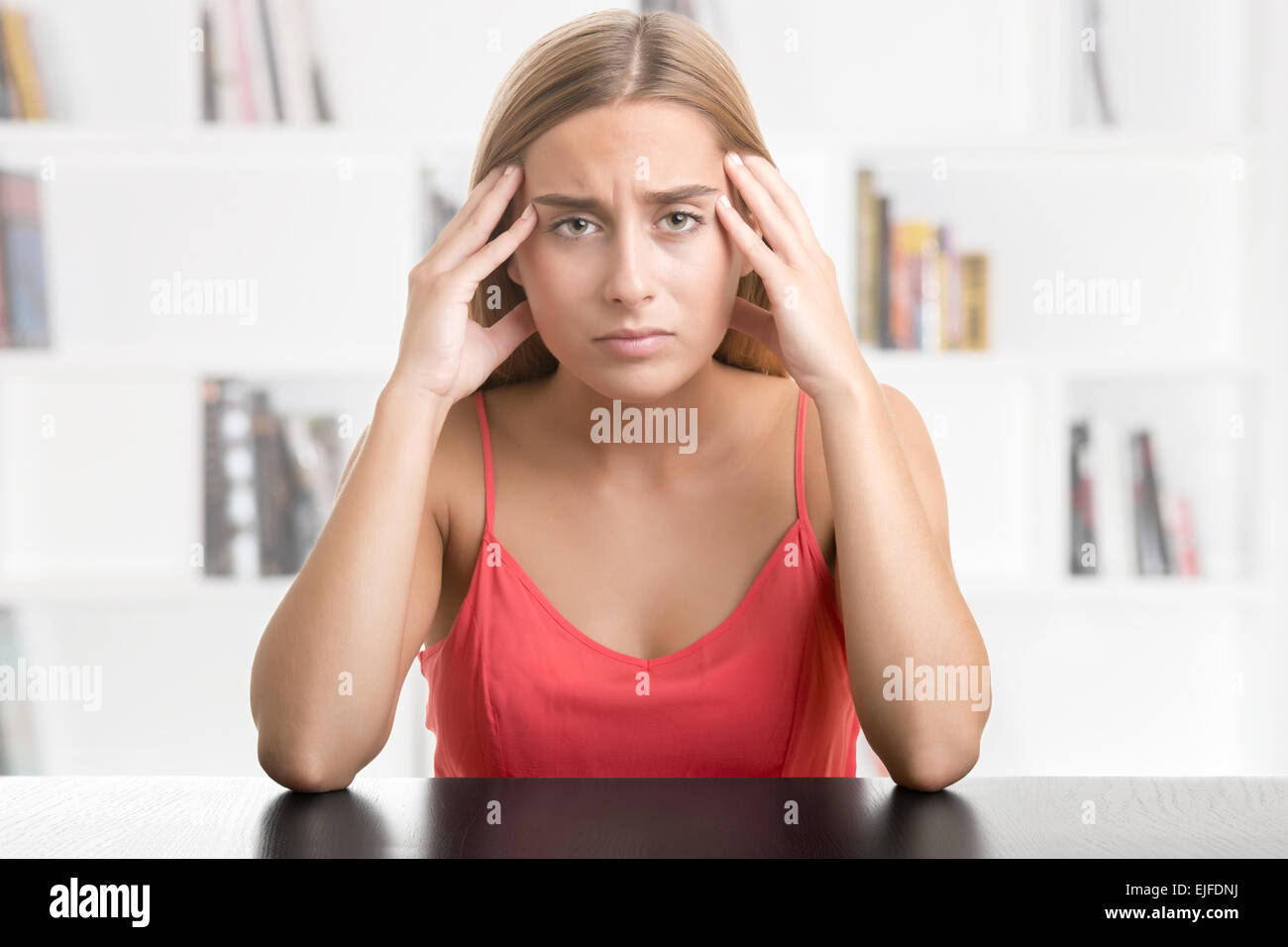 La donna che soffre di un mal di testa, tenendo la mano alla testa in una libreria Foto Stock