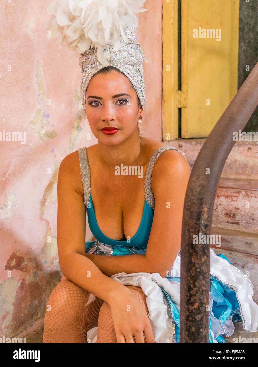 Una femmina ballerino cubano nel suo tradizionale costume di danza, compresi i copricapo, si siede sui gradini di un teatro e rivolta in avanti indietro Foto Stock