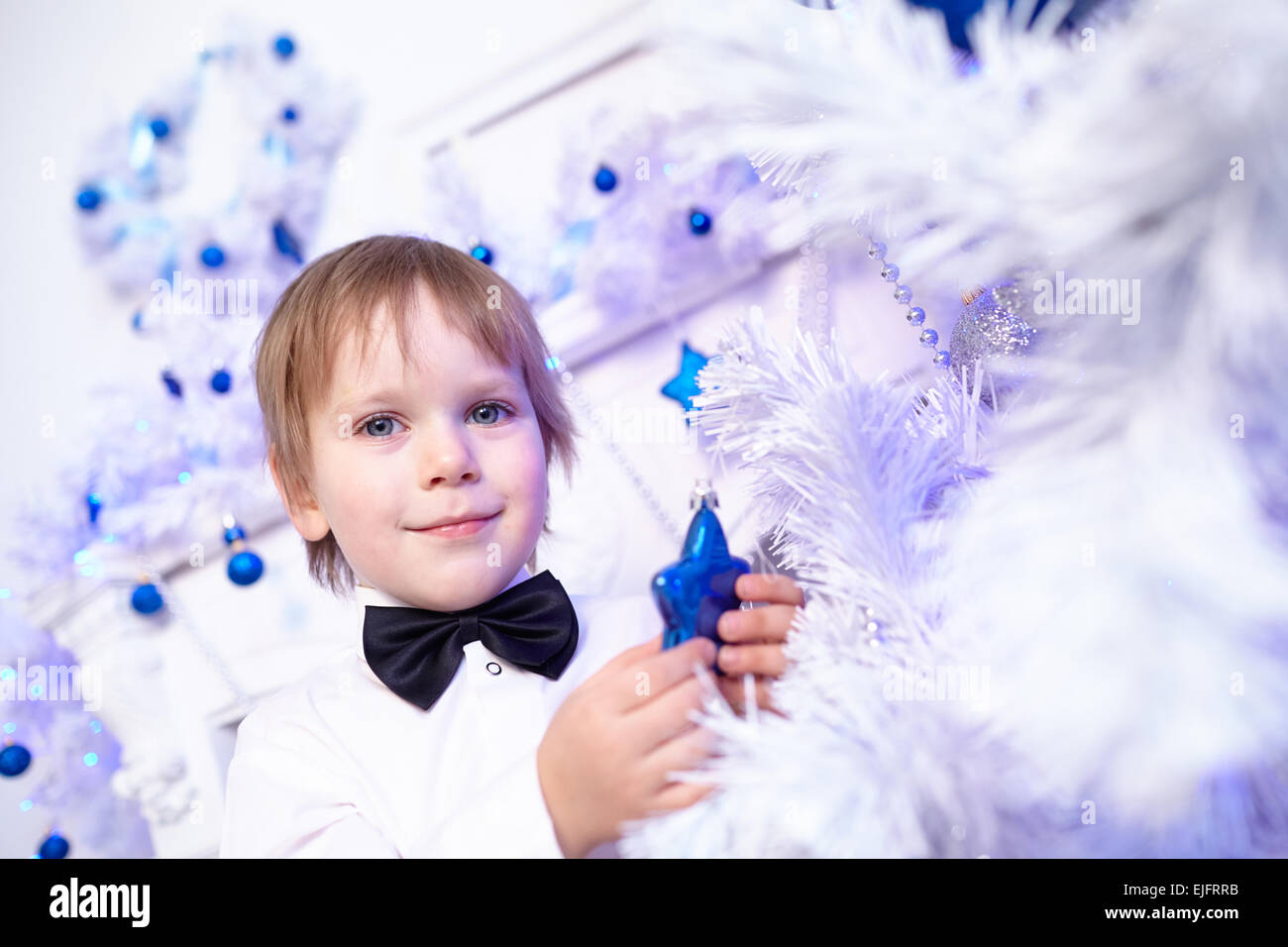 Little Boy in una camicia bianca ed il filtro bow tie decora un albero di Natale Foto Stock