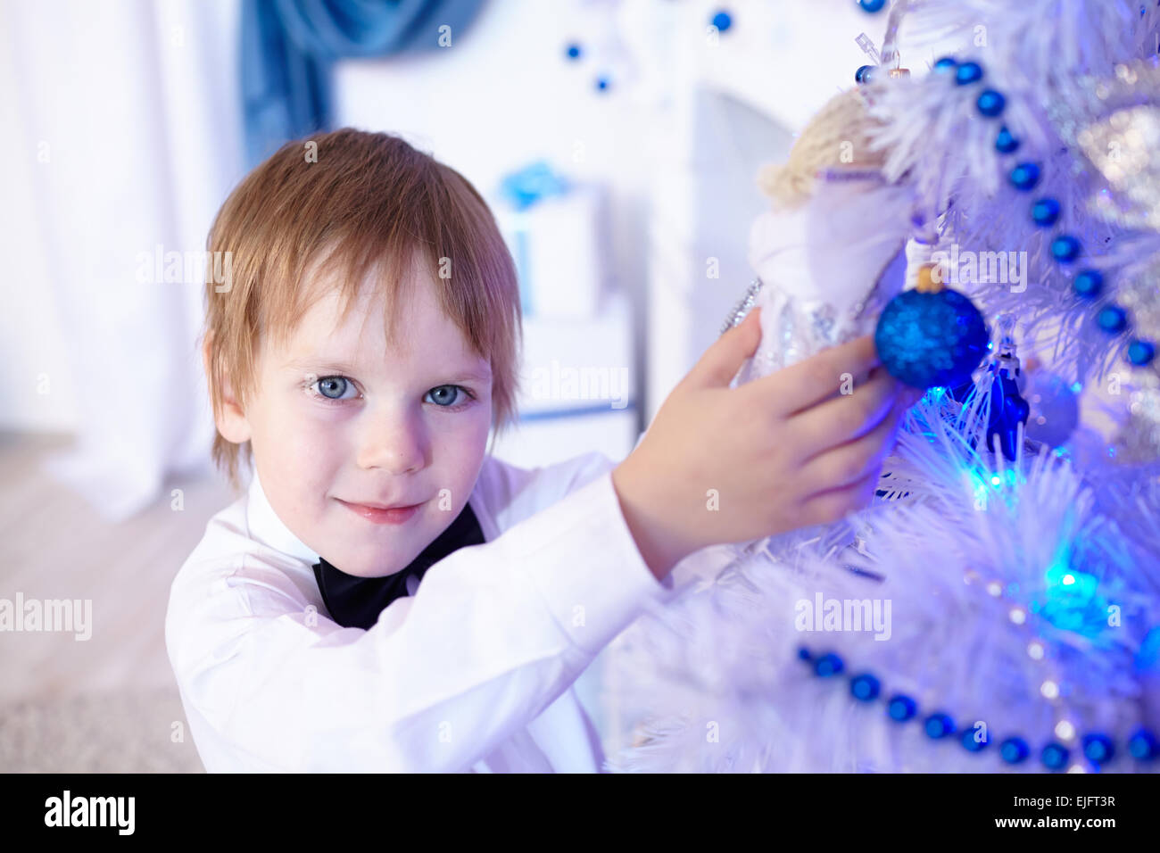 Little Boy in una camicia bianca ed il filtro bow tie decora un albero di Natale Foto Stock