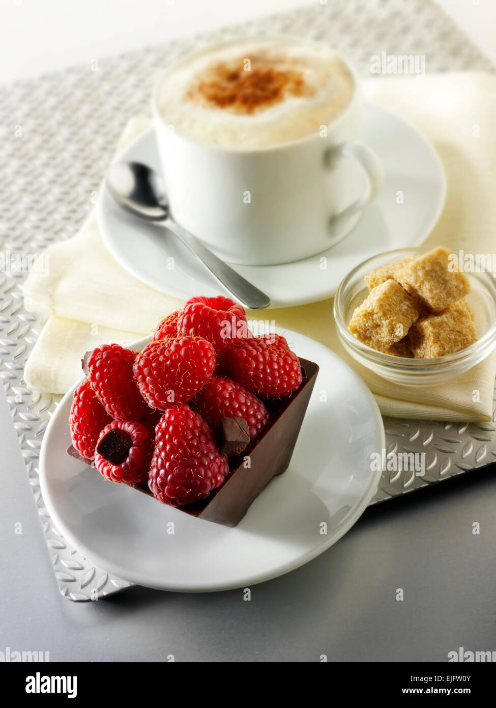 Una specialità di pasticceria fatta a mano ricca torta al cioccolato con scatola ripiena di lamponi freschi con caffè in un ambiente da tavola bianco Foto Stock
