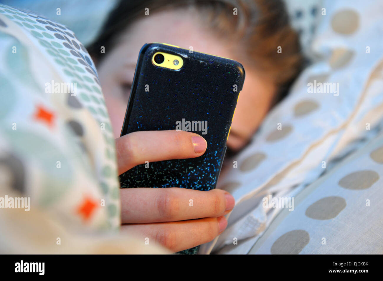 Ragazza adolescente utilizza il suo telefono cellulare di notte in letto. Foto Stock