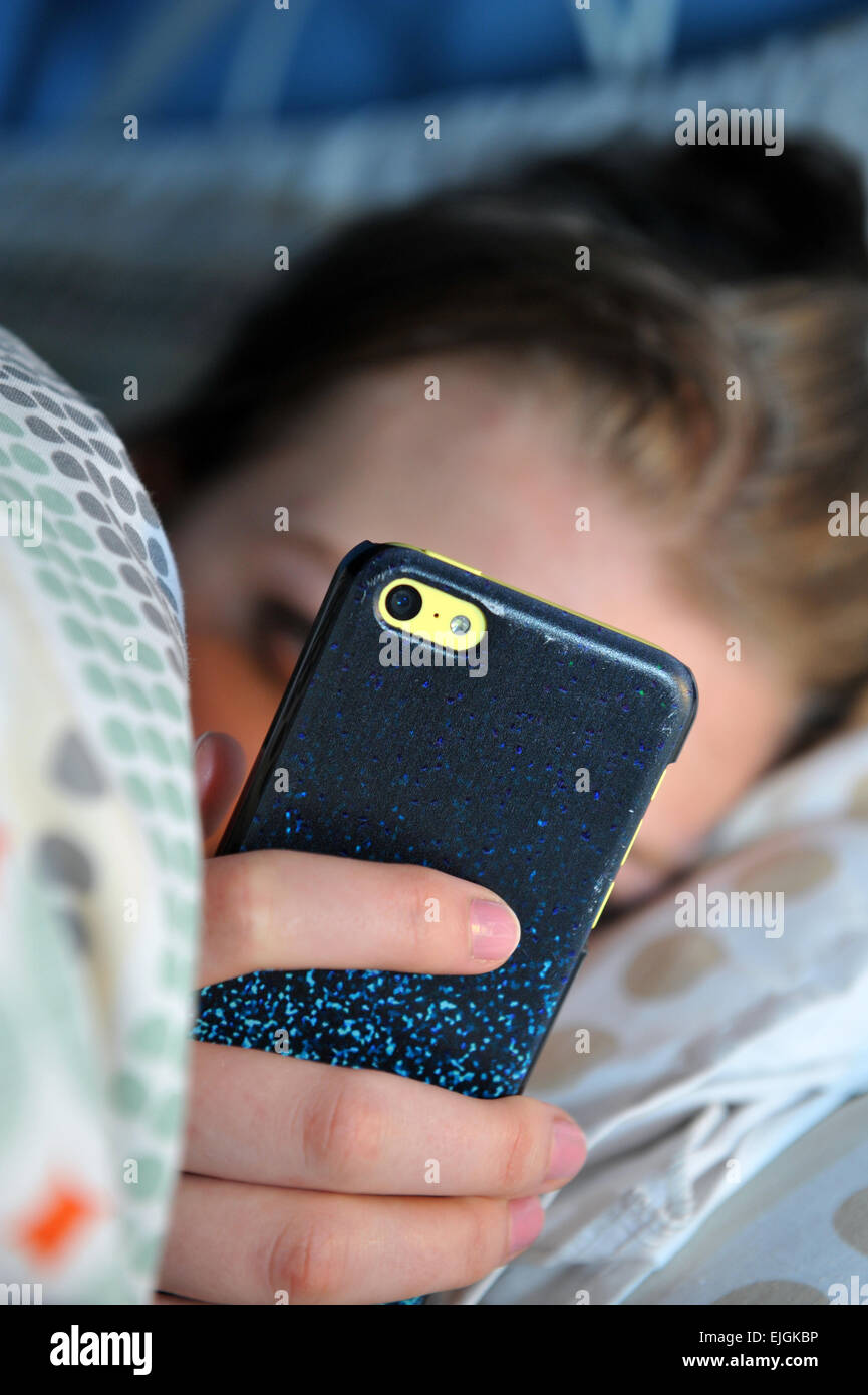 Ragazza adolescente utilizza il suo telefono cellulare di notte in letto. Foto Stock