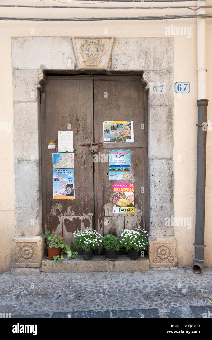Una vecchia porta di legno su un edificio dell'antica città di Cefalù Sicilia con poster incollato su di esso Foto Stock