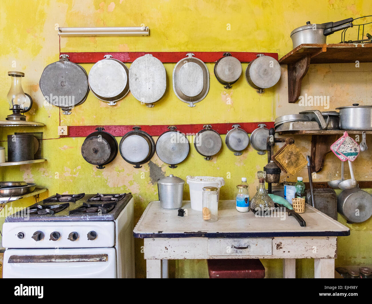 Una vista della stufa e tavolo di lavoro accanto ad essa e molte pentole e padelle appeso alla parete al di sopra di esse in una cucina di una casa cubana. Foto Stock