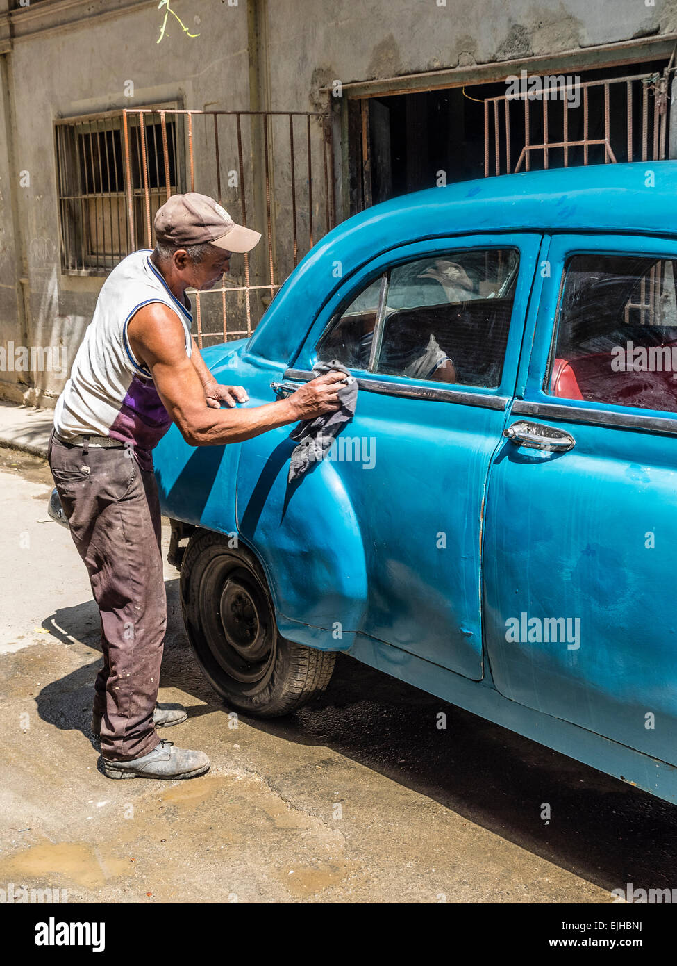 Un uomo afro-cubane pulisce la sua anni cinquanta turchese 4 porte Chevrolet automobile al di fuori nella Habana Vieja. Foto Stock