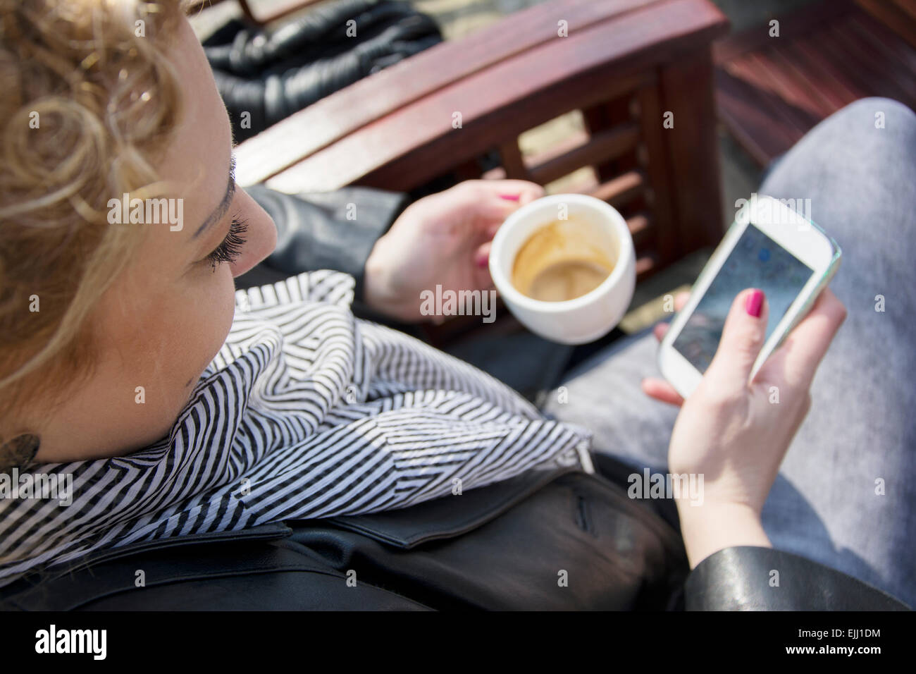 Piuttosto giovane donna bionda con capelli ricci seduto su una pausa caffè e digitando sul telefono.ella è di bere il caffè e sorridente come Foto Stock