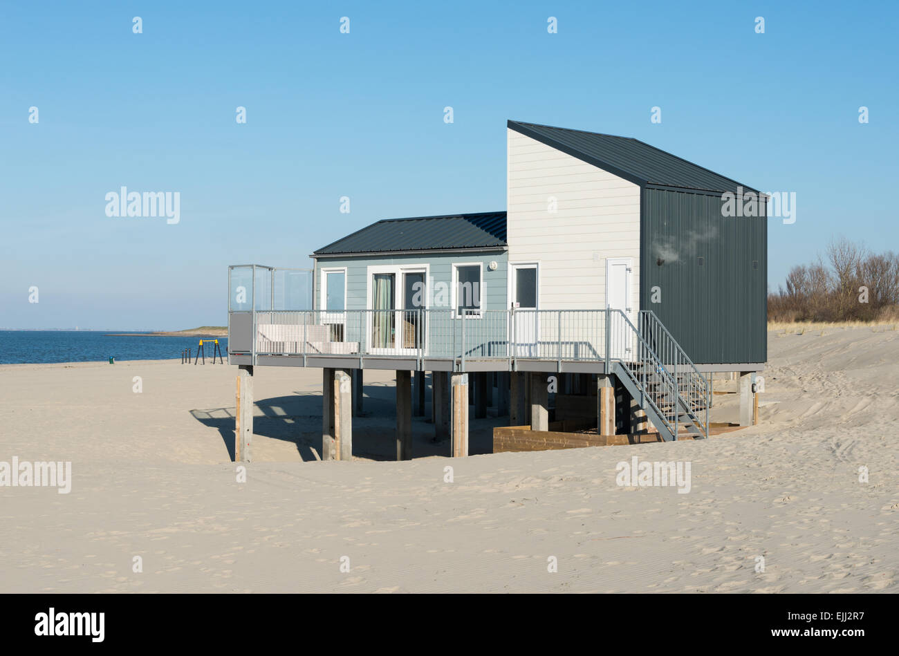 Spiaggia di legno casa per le vacanze sulla sabbia vicino al blu mare acqua in Olanda con le dune come sfondo Foto Stock
