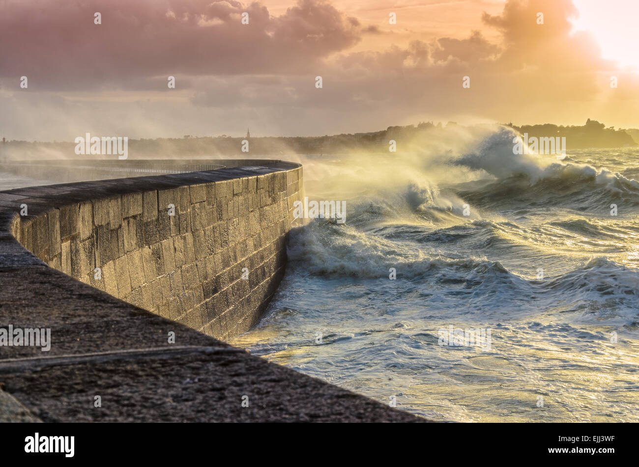 Grandi onde frantumazione su pietra ricurva Pier, sul maltempo con vivaci tramonto, grande marea, Saint Malo, Francia. Foto Stock