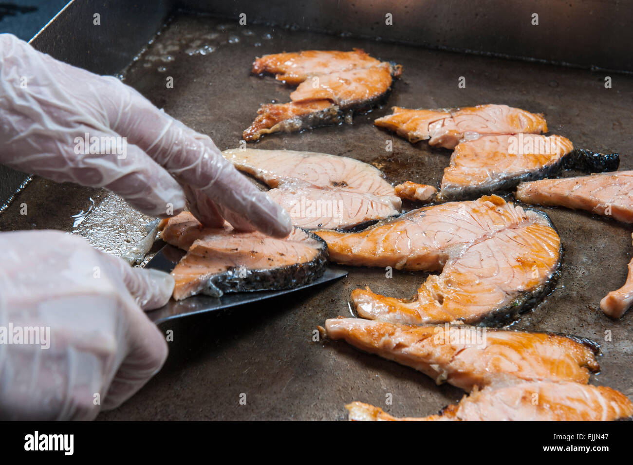 Filetti di Salmone con chef di cucina le mani sul grill piastra calda in un hotel e ristorante a buffet Foto Stock