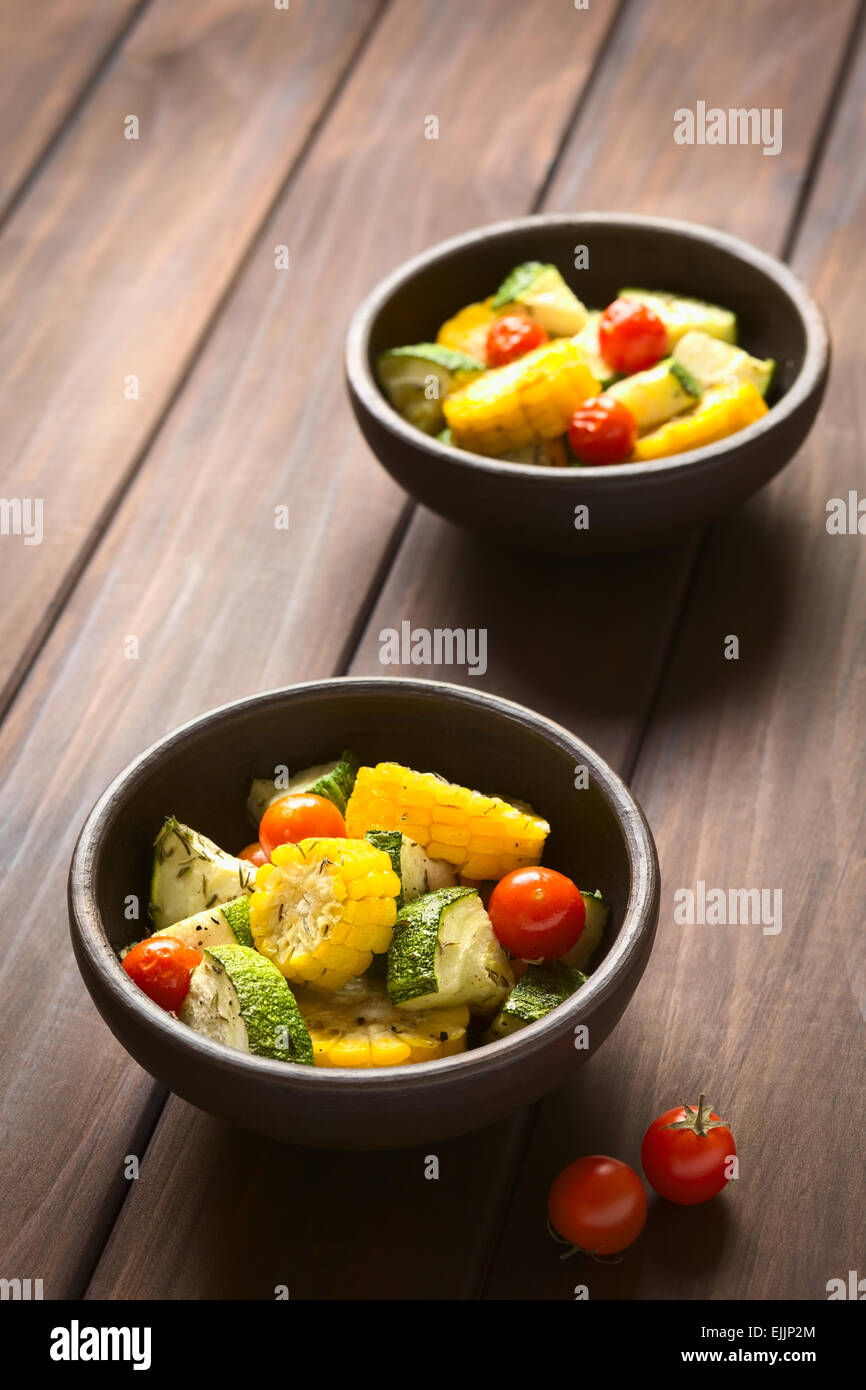 Due ciotole di verdura cotta di mais dolce, zucchine e pomodori ciliegia, condito con timo, fotografato in legno scuro Foto Stock