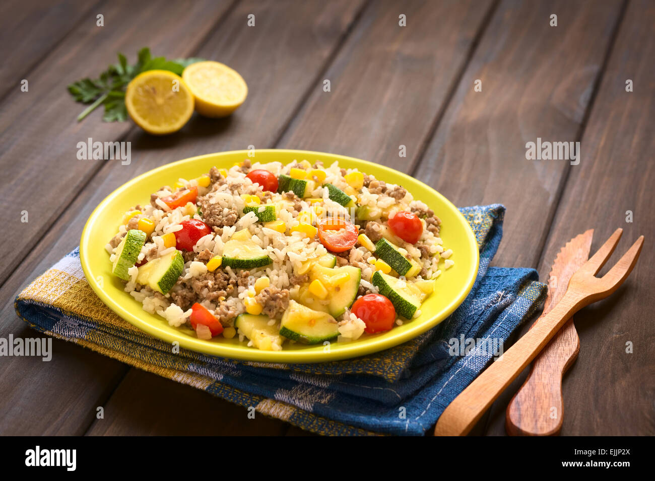 Piatto di riso con carne macinata e verdure (mais dolce, pomodoro ciliegino, le zucchine, la cipolla) servita su piastra in legno con coltello e forchetta Foto Stock