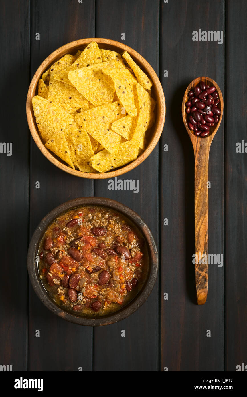 Tettuccio di colpo di chili con carne e tortilla chips in ciotole con fagioli secchi borlotti sul cucchiaio di legno, fotografato in legno scuro Foto Stock