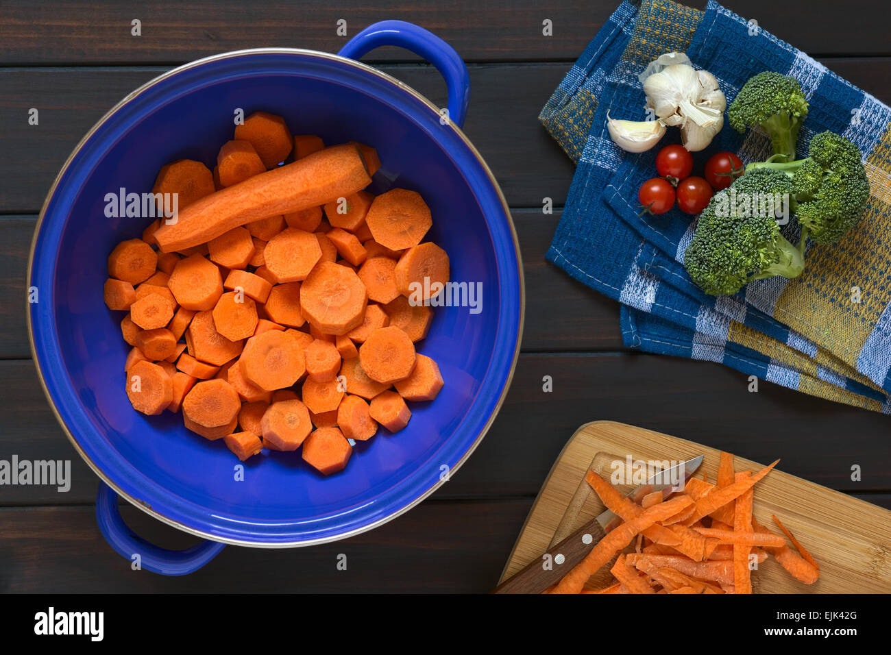 Tettuccio di colpo di crudo fresco di carote tagliate a fette in blu il filtro di metallo con broccoli, cherry pomodoro aglio e bucce di carota accanto Foto Stock