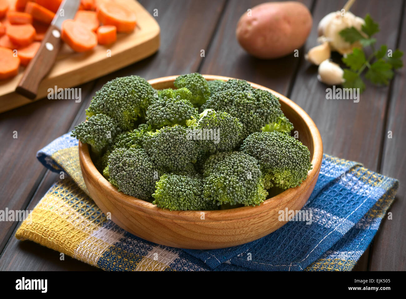 Crudo fresco cime di broccoli in ciotola di legno con fette di carota sulla tavola di legno, patata, aglio e prezzemolo nel retro Foto Stock