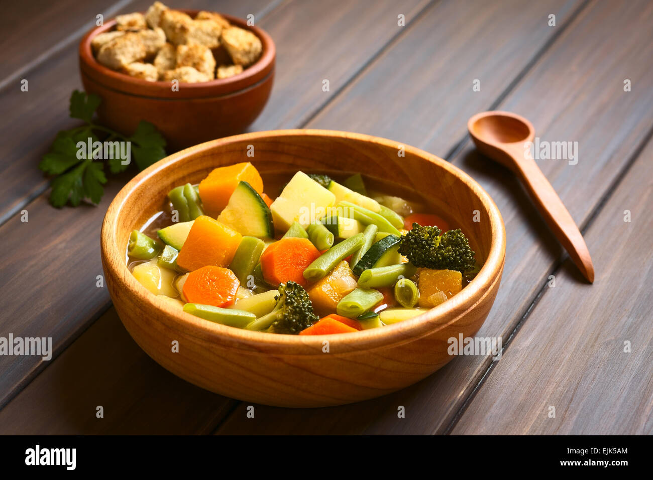 Ciotola di legno di origine vegetale zuppa di zucchine, verde fagiolo, carote, broccoli, patate e zucca con una piccola ciotola di crostini Foto Stock