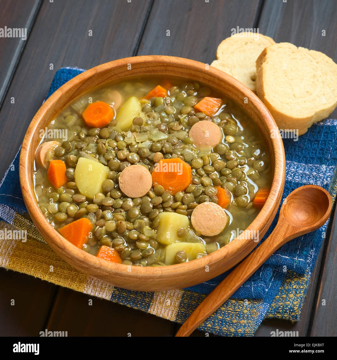 Ciotola di legno di zuppa di lenticchie fatta con la patata, la carota e la cipolla e le fette di salsiccia, fotografato in legno scuro con luce naturale Foto Stock