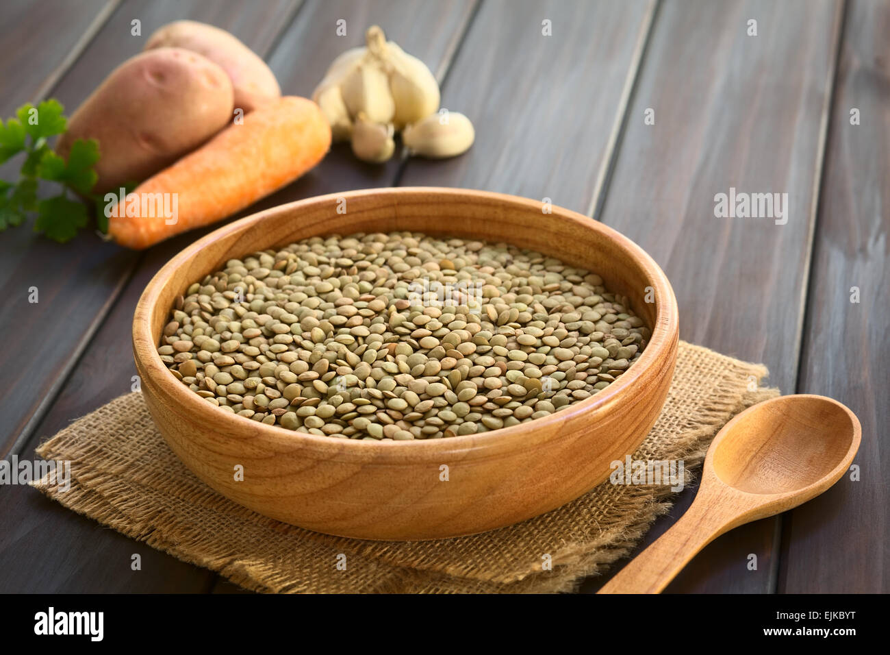 Materie lenticchie (lat. Lens culinaris) nella ciotola di legno con verdura cruda (patata, carota, aglio) nella parte posteriore Foto Stock