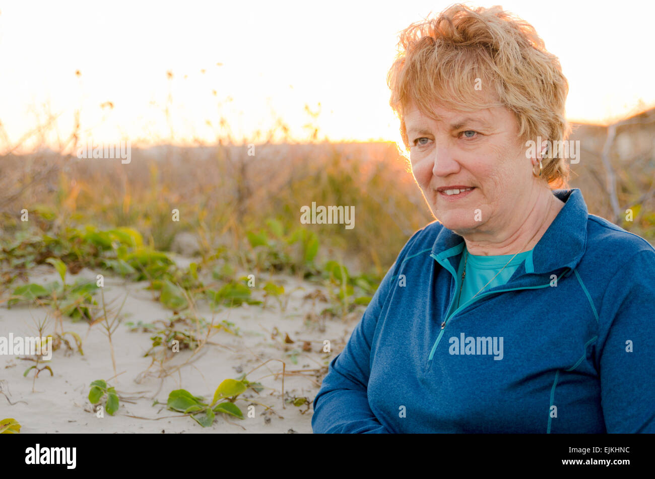 Senior età femmina 60-65 piedi con il sole per il suo ritorno in dune di sabbia vicino alla spiaggia cercando rilassati e felici Foto Stock