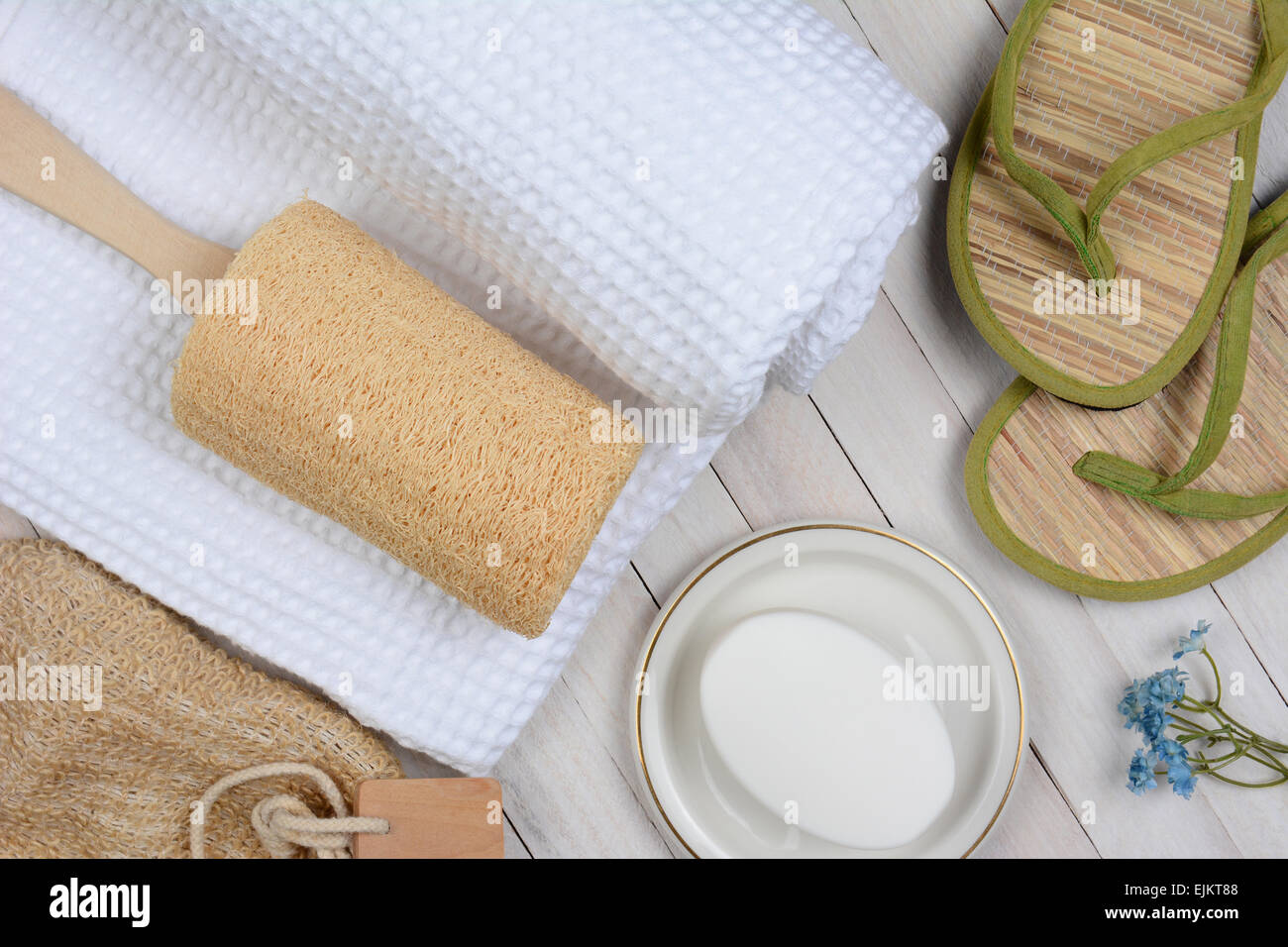 Spa e il bagno ancora in vita. Alta angolazione degli accessori per il bagno tra cui, asciugamani, sapone, loofah e sandali, su un rustico bianco Foto Stock